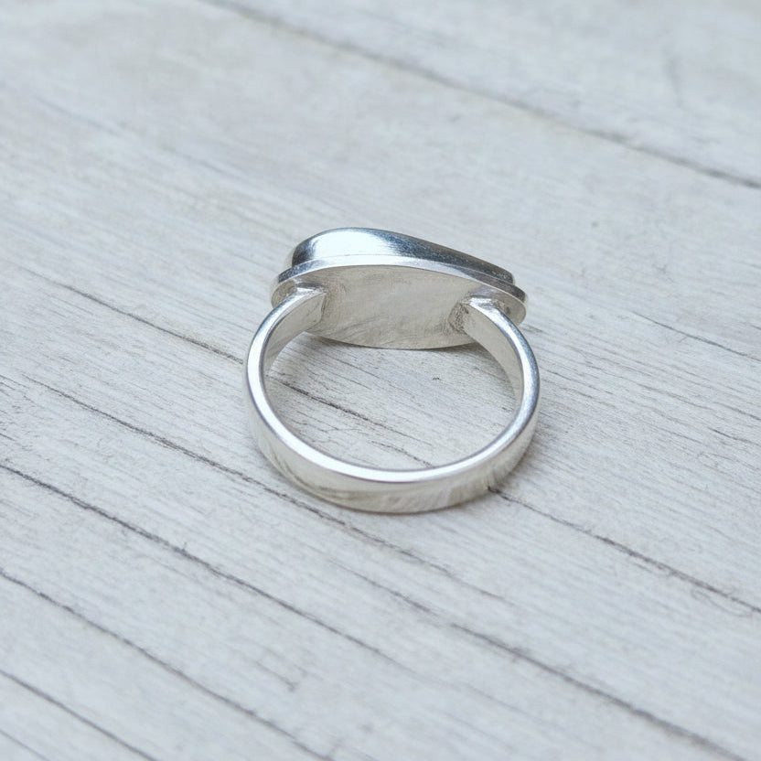 A polished silver ring with a textured, hammered finish resting on a light gray, weathered wooden surface.