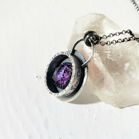 Faceted amethyst stone and sterling silver shadow box pendant with stamped leaves. Necklace is 18 inches long.