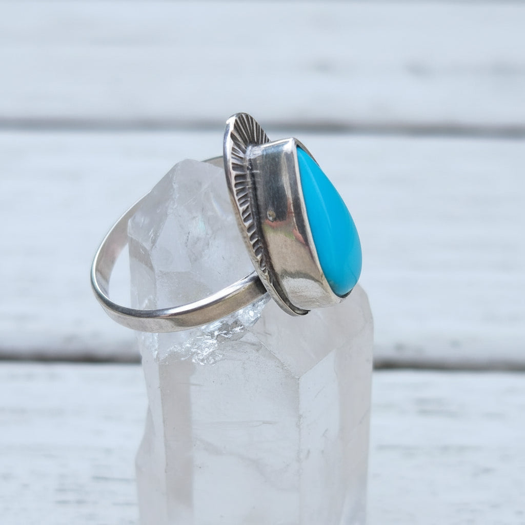 Silver ring with a turquoise stone on a clear crystal on a wooden surface