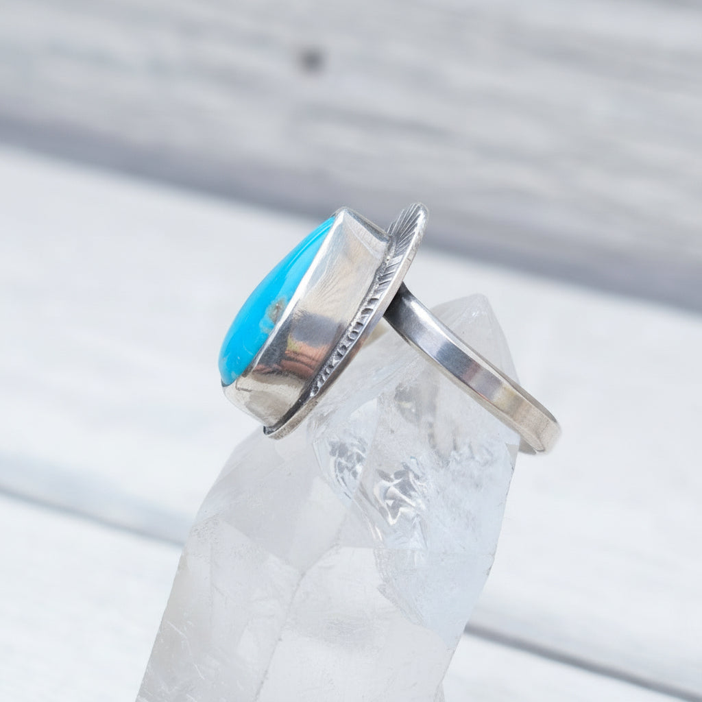 Silver ring with a blue stone on a clear crystal on a wooden surface